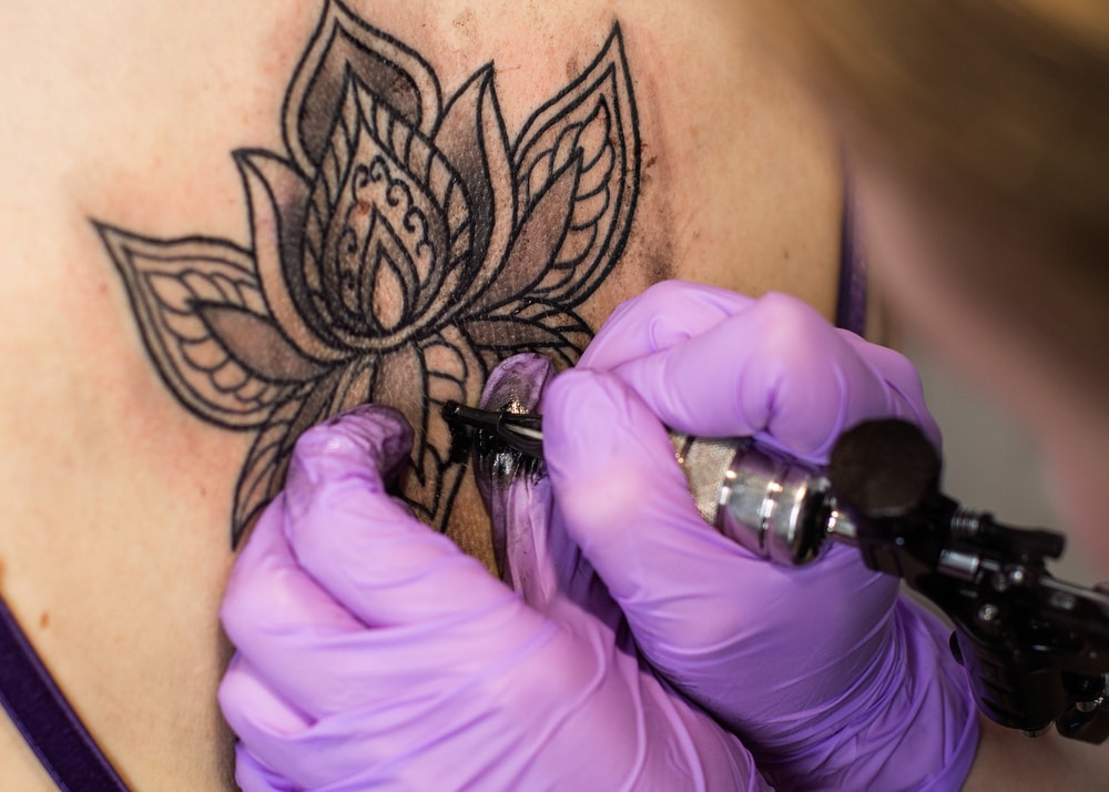 Tatuando un motivo de flor de loto en blanco y negro en una espalda