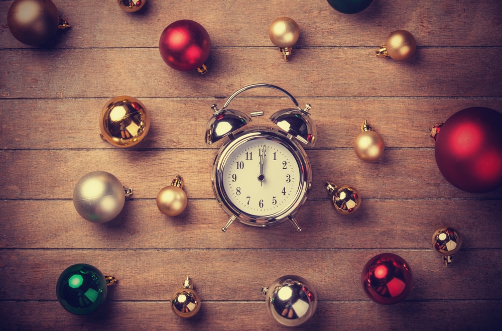 Un reloj despertador en una mesa de madera rodeado de bolas navideñas de colores