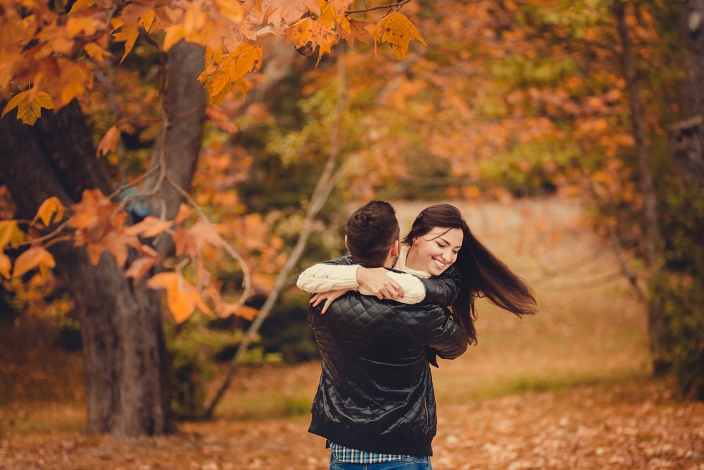 Una pareja se abraza en medio de un parque lleno de hojas de otoño