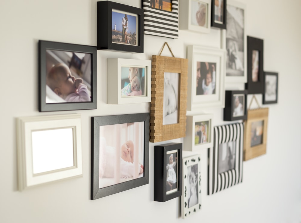 Una pared blanca llena de cuadros con fotografías familiares en marcos de diferentes estilos