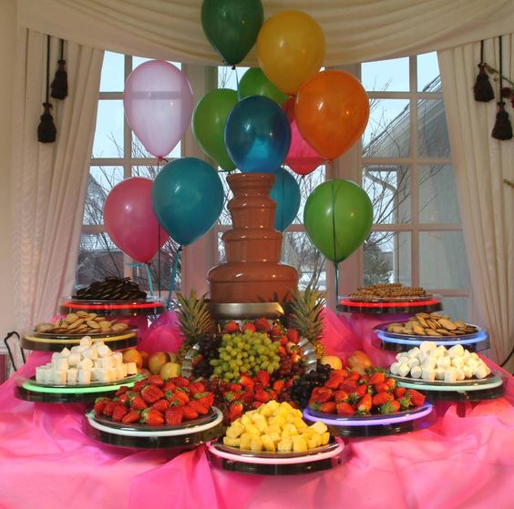 Una mesa decorada presidida por una fuente de chocolate y comida para bañar en ella