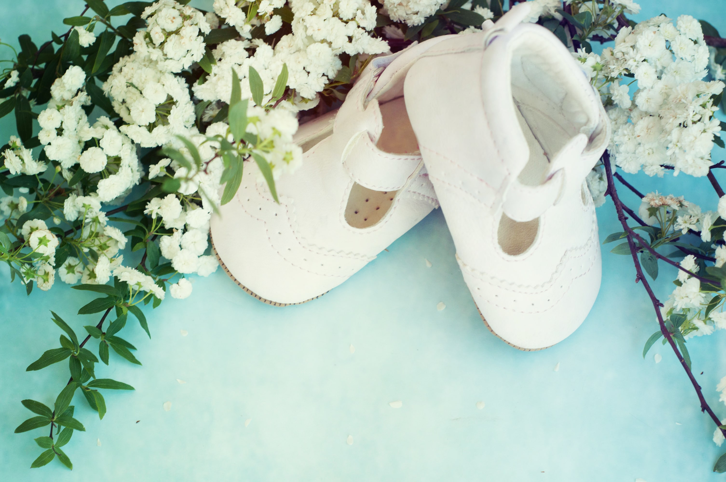 Zapatitos blancos de bebé con flores blancas sobre mesa azul
